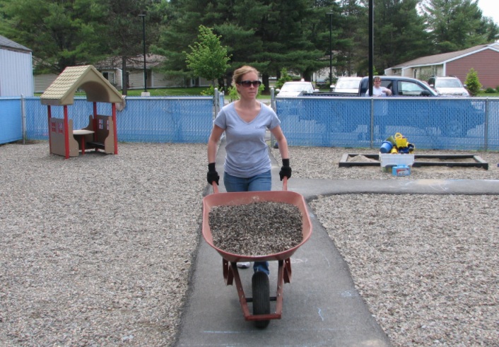 CEO Kara Hay lending a hand with a wheelbarrow full of rocks to help establish a new Child Development Head Start location, showcasing hands-on leadership.